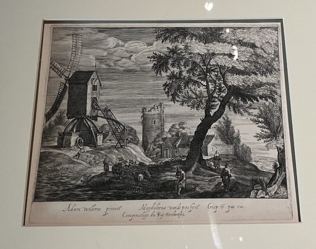 A black and white engraving with a mill sitting on a slight rise, next to a tree surrounded by five human figures holding long handled tools, and some sheep. There is a house in the background with a tower nearby.