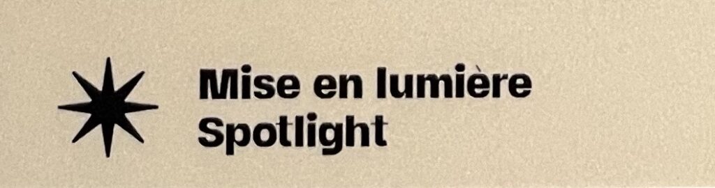 Portion of a "Spotlight" label, with an 8-point star and text in black or navy blue, on a yellow background, reading "Mise en lumière / Spotlight"