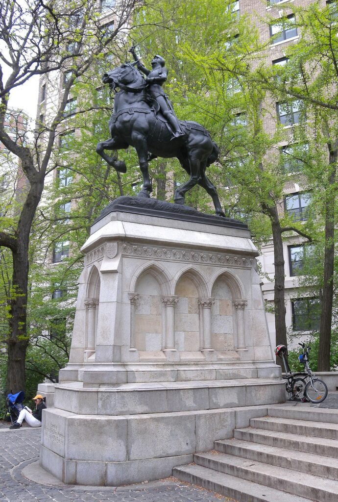 Photo of a black-colored statue of Joan of Arc on a horse, which sits atop an elaborate white stone plinth next to a set of 6 white stone stairs.