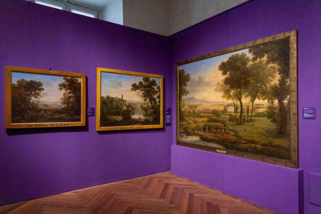 Installation view of landscape paintings against purple walls.