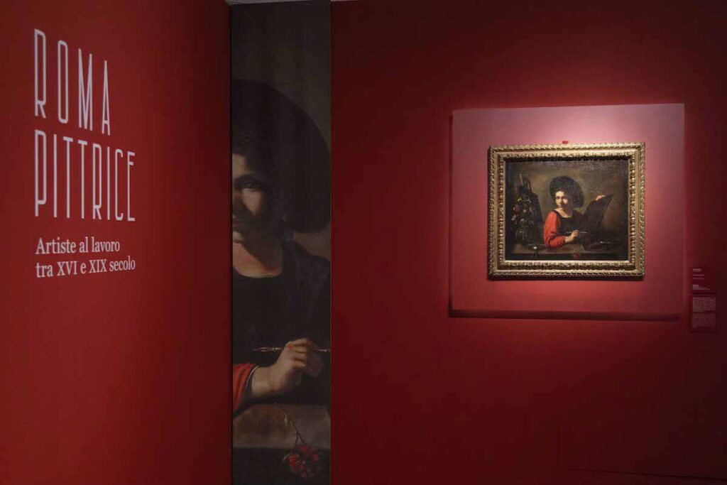 Installatiion view showing title of exhibition at left, and a painting of a young woman at an easel, tower the right.