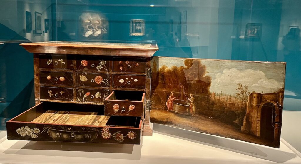 A floral still life appears when all ten drawers are closed. (There are three rows of three smaller drawers, underneath which is one long shallow drawer.) A scene on the inside of the hinged door depicts the biblical story of Christ and the Samaritan woman. An architectural painting of the interior of a church appears in the bottom drawer. The rest of the drawers contain portraits of prominent religious reformers such as John Calvin and Martin Luther. 